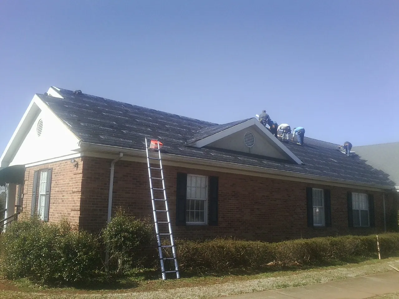 Crew tearing shingles off a brick ranch roof with a ladder set — Metal Roof Repair work by our crew in Custer City