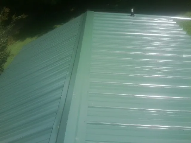 New green metal panels meeting at the ridge of a roof — Flat Roof Repair work by our crew in Custer City