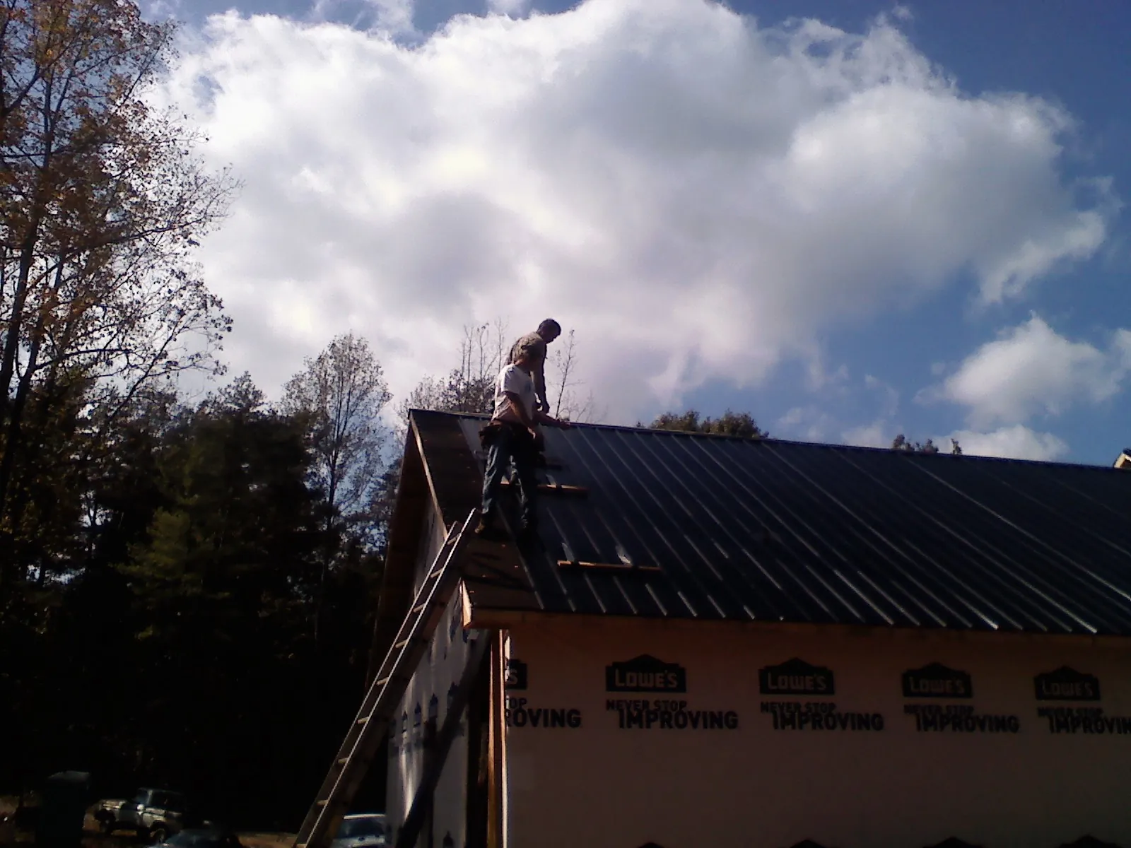 Roofer fastening dark metal panels high against a cloudy sky, from a Roof Inspection job in Custer City
