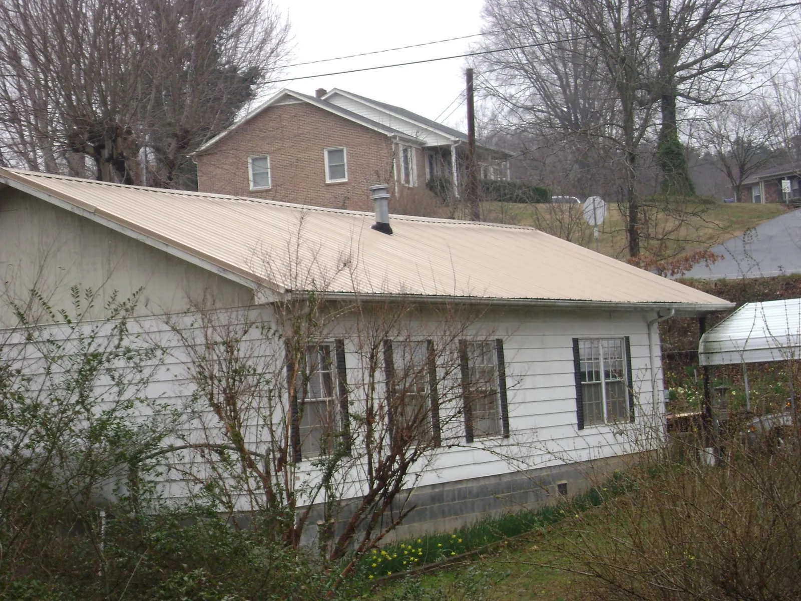 Tan metal roof on a white sided house set into a hillside — Commercial Roofing by Roofing Brothers in Custer City